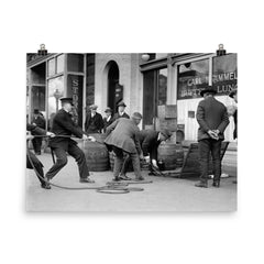 Police seizing bootleg liquor - Police haul barrels of illegal liquor from the basement of a speakeasy during the era of alcohol prohibition, 1923 poster on a plain backdrop in size 8"x10".