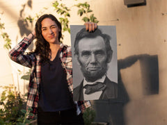 Young woman winking and holding up an Abraham Lincoln poster print.