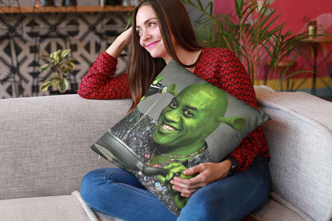A young woman on a sofa holding an Ainsley Harriott Shrek throw pillow and trying not to laugh.