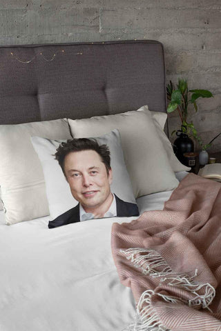 An Elon Musk pillow on a bed with a white duvet.