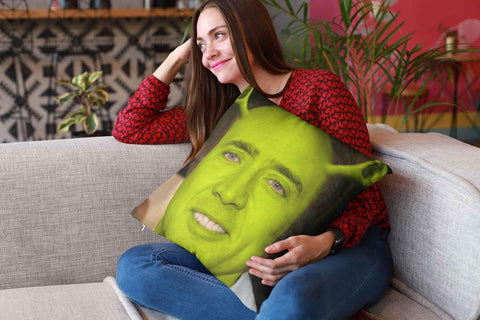 A young woman on a sofa holding a Nicolas Cage Shrek pillow and trying not to laugh.
