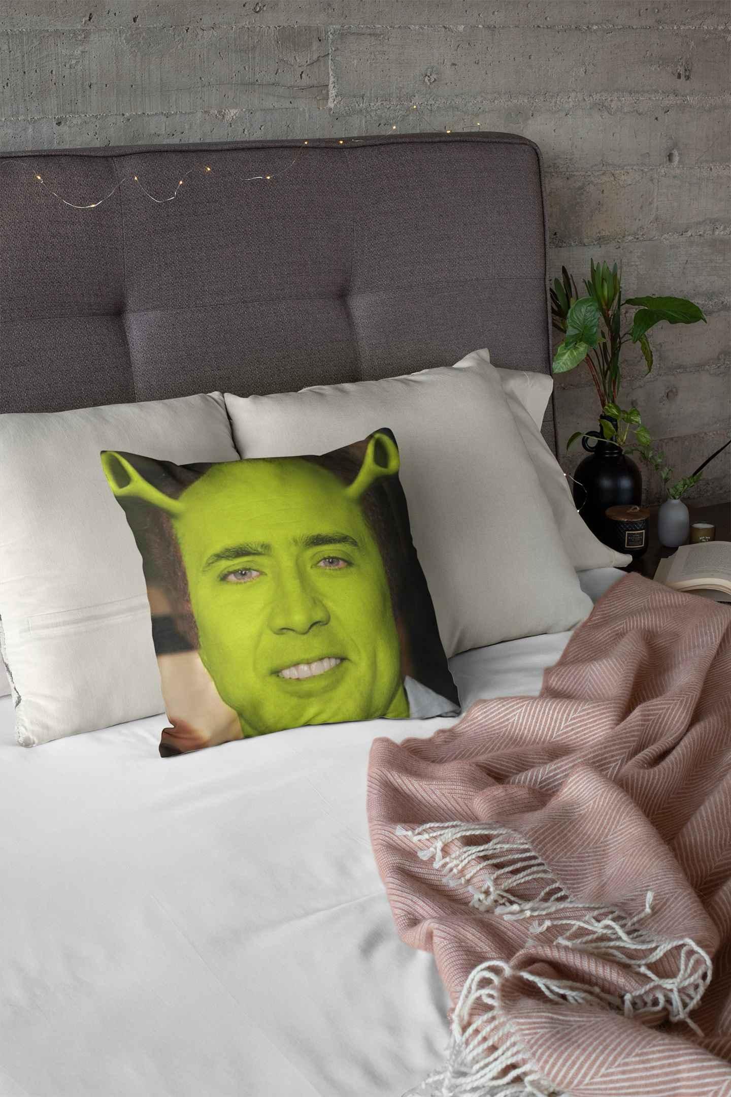 A Nicolas Cage Shrek pillow on a bed with a white duvet.
