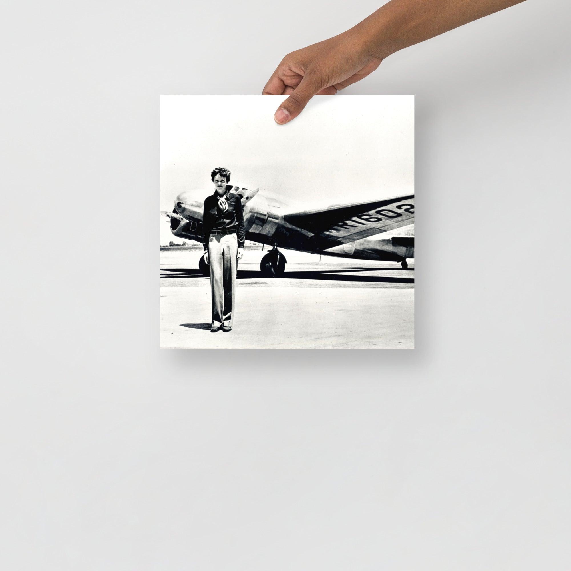 An Amelia Earhart standing in front of the Lockheed Electra on a plain backdrop in size 12x12”.